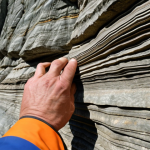 **A geologist in the Ardennes, examining folded rock layers. Close-up on the rock face showing intricate folds and faults, demonstrating the immense forces of geological activity.**